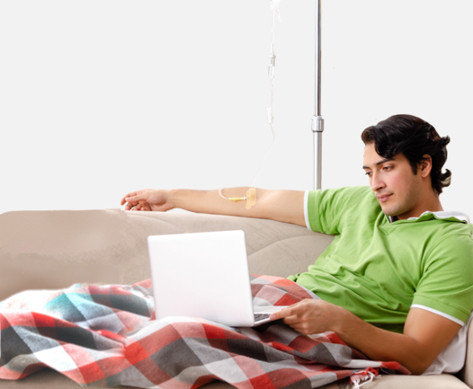 An iMCD patient sitting on a couch receives their Sylvant infusion at home.